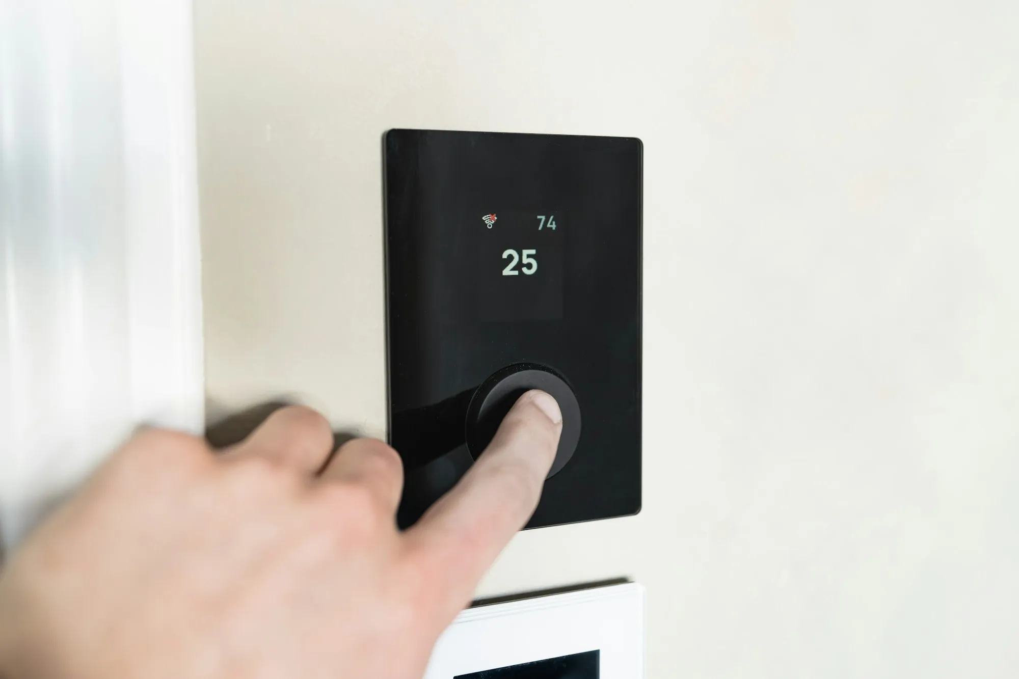 Hand adjusting a black wall thermostat