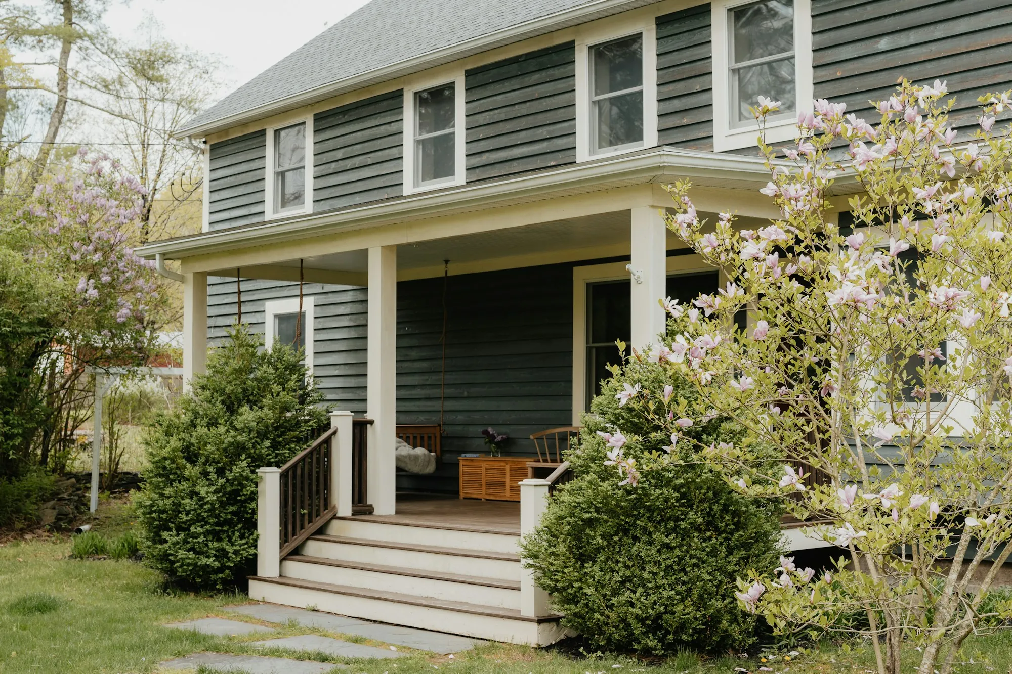 Gray sided house with a porch and spring trees