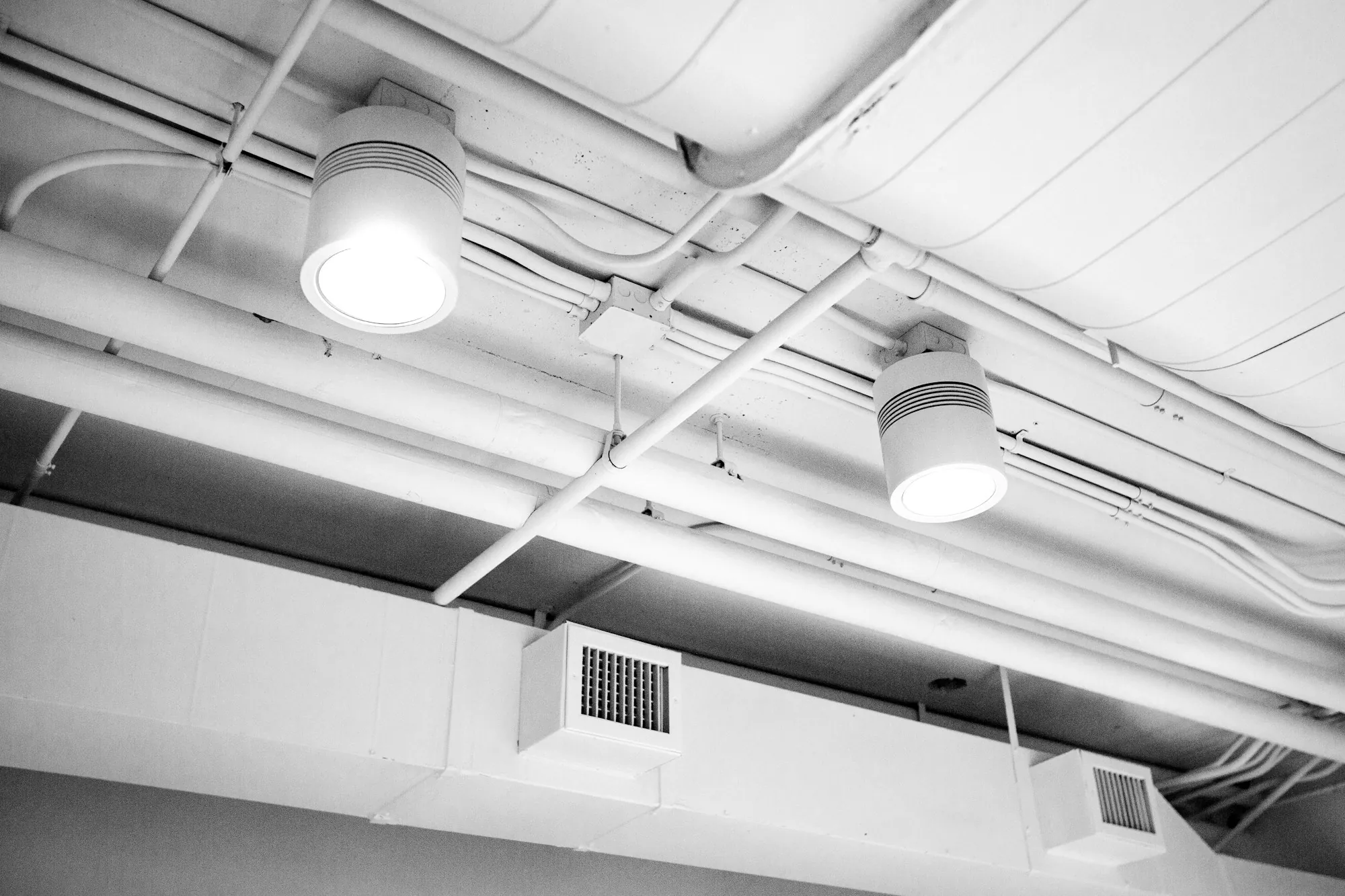 Exposed white ductwork with vents in an office ceiling
